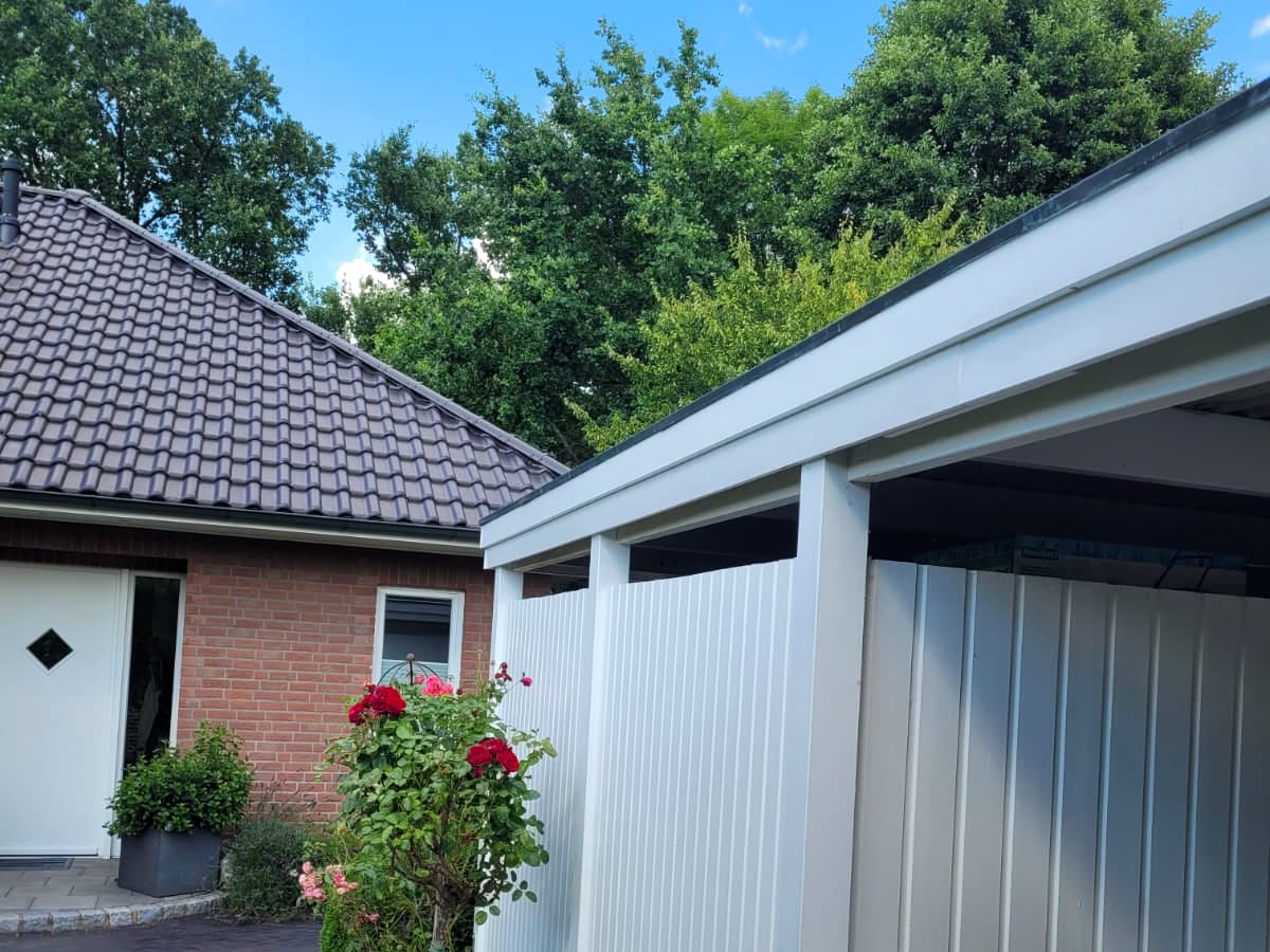 Weißer Carport mit integriertem Abstellraum neben einem Wohnhaus