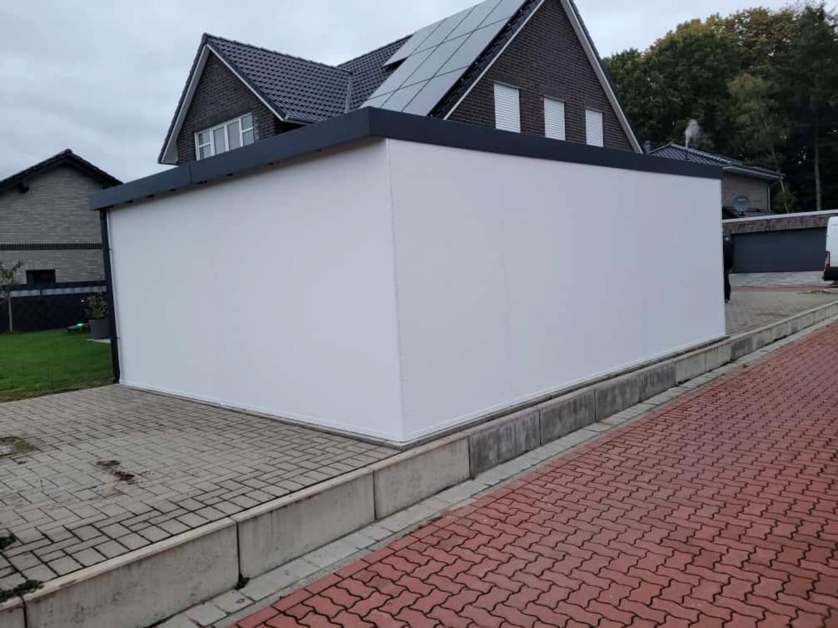 Weiße Fertiggarage mit Flachdach neben einem Einfamilienhaus