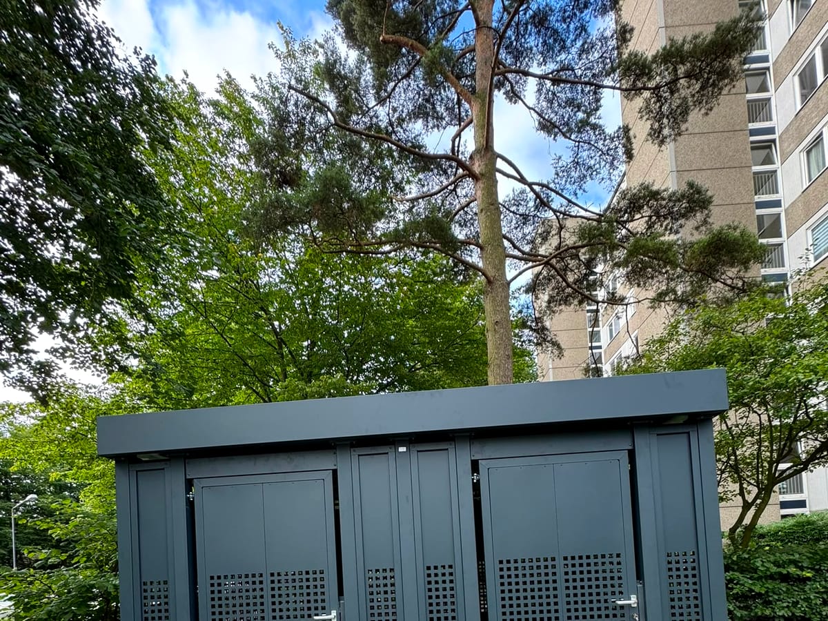 Metall-Müllhaus mit zwei Türen vor einem Mehrfamilienhaus